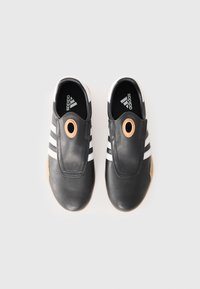 Black leather shoes with white stripes and a circular accent on the upper, featuring a gum sole and a sleek, streamlined design.