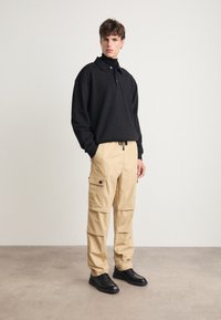 Svart fleece genser med krage og knappeåpning, kombinert med lysebeige cargo-bukser med klafflommer, brukt med svarte sko.