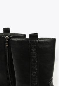 Black leather ankle boots with a smooth texture, a side zipper, and a branded vertical strap detail on the upper.