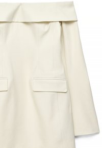 Kremowa sukienka z odkrytymi ramionami i długimi rękawami, z dwoma płaskimi kieszeniami oraz subtelnymi plisami na górnej części. Gładka tekstura.