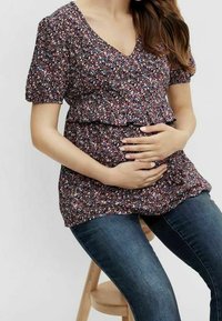 Blusa per maternità con motivo floreale, scollo a V e maniche a palloncino corte, realizzata in tessuto scuro. Abbinata a jeans blu aderenti. Silhouette rilassata.