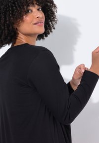 Musta pitkähihainen paita rentoa leikkausta, pyöreä pääntie ja sileä pinta. Näkyvät sauman yksityiskohdat hihoissa ja hartioilla.