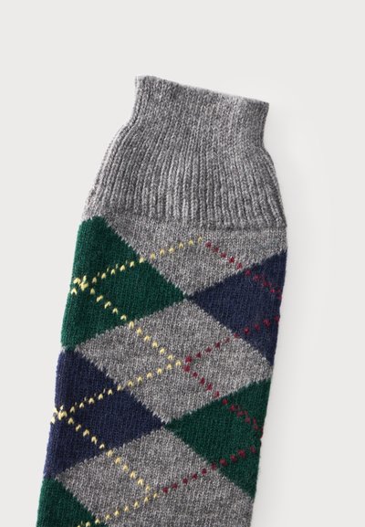 Chaussette en laine tricotée avec un bord-côte gris et un motif losanges en vert, bleu marine, jaune et rouge sur fond gris.
