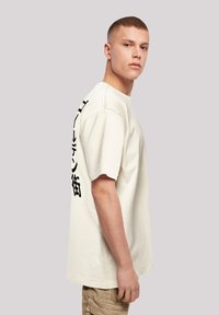 Helle Baumwoll-T-Shirt mit kurzen Ärmeln, das schwarzen Text an der linken Seite trägt. Der Stoff ist weich und locker im Schnitt.