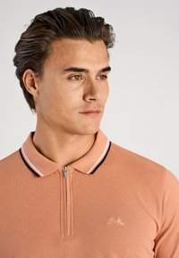 Koszulka polo z krótkim rękawem w kolorze koralowym z kołnierzem na zamek, kontrastowymi granatowymi i białymi paskami oraz subtelnym logo wyszytym na piersi.