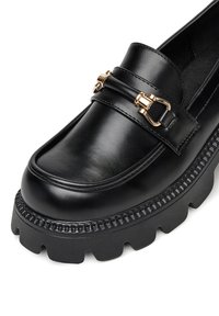 Černé kožené mokasíny s robustní gumovou podrážkou, se zlatým kovovým detailem a hladkým povrchem na svršku.
