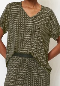 Top de manga corta en verde oscuro con escote en V y un estampado floral. Tejido ligero con un corte holgado, combinado con pantalones de estampado y un cinturón negro.