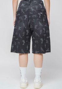 Shorts de mezclilla negra con un patrón impreso de varios símbolos e iconos. Detalle de dobladillo sin acabar, bolsillos traseros y una etiqueta de marca sutil.