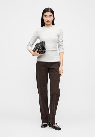 Hallikas soonikko pikkade käistega pluus, mis on kombineeritud pruuni sirge lõikega pükstega. Modell hoiab käes musta tekstuurse õlakoti, millel on kuldsed õmblused. Välimuse lõpetavad mustad madalad kingad.