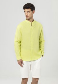 Limoengroen linnen shirt met een bandkraag, lange mouwen en een knoopsluiting aan de voorkant. Draagt met witte shorts, die een gladde textuur hebben.