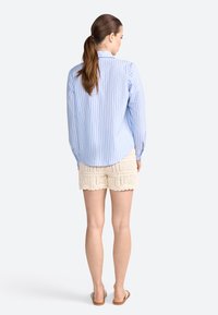 Lichtblauw gestreepte button-up shirt met lange mouwen, gecombineerd met crèmekleurige gehaakte shorts met een gegolfde zoom. Eenvoudige sandalen.