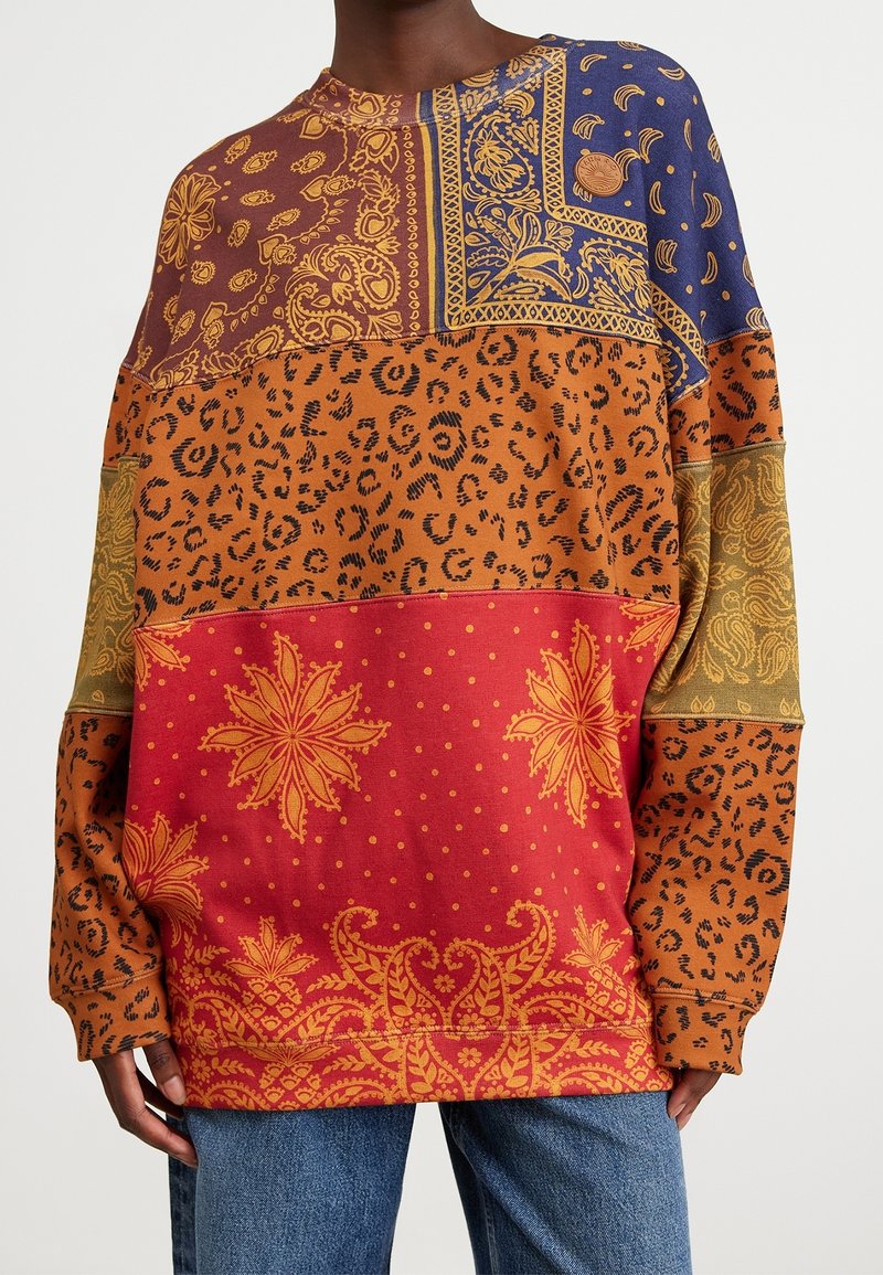 Sudadera extragrande con una mezcla de tejidos en naranja, azul y rojo. Presenta intrincados patrones de paisley, flores y estampado de leopardo. Textura de mezcla de algodón.