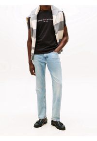 Czarny t-shirt z logo "TOMMY HILFIGER", jasnoniebieskie jeansy o prostych nogawkach, szaro-kremowy sweter w paski zarzucony na ramiona, czarne loafersy.