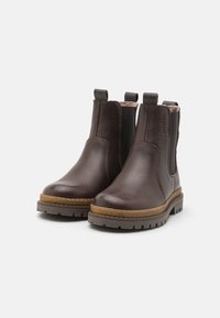 Bottines Chelsea en cuir marron avec des panneaux latéraux élastiques, semelle en caoutchouc et piqûres contrastées. Équipées de languettes de tirage pour un enfilage facile.