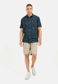 Marineblauw overhemd met korte mouwen, voorzien van geometrische patronen, knoopjesontwerp, borstzak, gecombineerd met licht kaki shorts en witte sneakers.