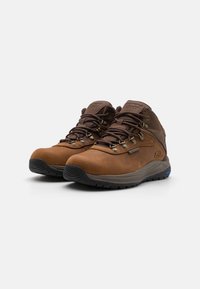 Botas de senderismo marrones impermeables con diseño de caña alta, ojales de metal para los cordones y suelas de goma texturizadas para tracción. Diseño simple y material duradero.