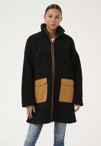 Zwart fleece jack met een volledige rits, hoge kraag en twee beige zakken van stof. Heeft een gestructureerde stof en contrasterende ritsdetails.