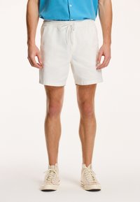 Hvide bomulds shorts med elastisk talje og snøre, med en afslappet pasform og opkrøllede kanter. Parret med beige høj-top sneakers.