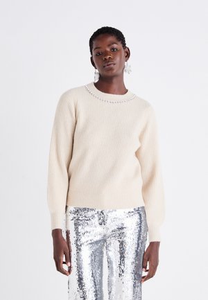 Beige ribbed sweater with a round neckline adorned with a silver bead detail, paired with shiny silver sequin pants.