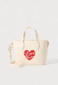Cream-colored handbag made of faux leather, featuring a red heart-shaped patch with "Love Moschino" text. Gold-tone hardware accents and detachable strap.