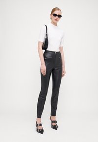 Svarta faux läderbyxor med dragkedjefickor, i kombination med en åtsittande vit topp och svarta klackskor. Accessoarerna inkluderar solglasögon och en liten väska.