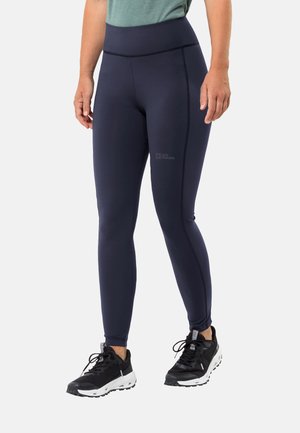 Marineblauwe leggings van rekbaar materiaal, met een hoge tailleband en naaddetails. Combinatie met zwarte sportschoenen met witte zolen.