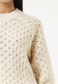 Brede trui in crème met een textuur, diamantpatroon. Kenmerkend is de geribbelde ronde halslijn en de ontspannen pasvorm met een zachte, comfortabele stof.