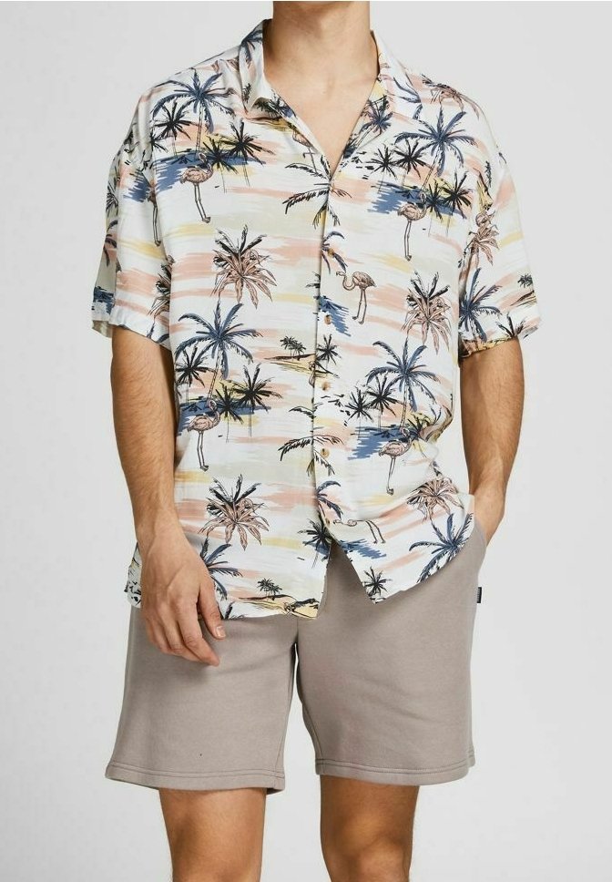 Camicetta a maniche corte in tessuto leggero con stampa tropicale di palme e fenicotteri in colori pastello, abbinata a pantaloni beige.