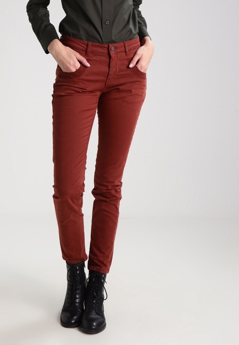 Red slim-fit pants made of smooth fabric with front pockets and a button closure, paired with black lace-up ankle boots.