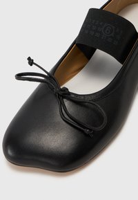 Černé kožené baletní ploché boty s kulatou špičkou, s dekorativní mašlí a širokým elastickým páskem přes vrchní část pro bezpečné uchycení.