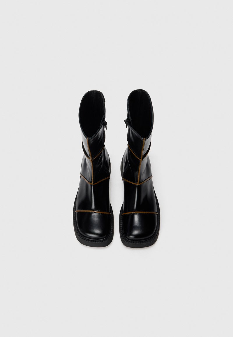 Svarta läderankelstövlar med kantig design, kontrasterande gul söm, fyrkantig tå och sidodragkedjor för enkel på- och avtagning.