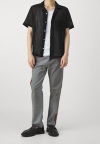 Maglietta nera a maniche corte in rete, T-shirt bianca sotto, jeans grigi con strisce laterali arancioni e mocassini neri. Dettagli semplici con bottoni.