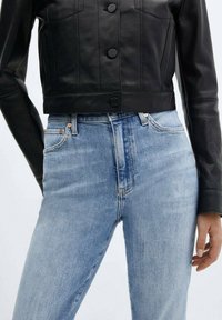 Black leather cropped jacket with button closure and structured seams, paired with light blue high-waisted denim jeans featuring a slight fade.