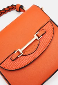 Pomarańczowa skórzana torebka na ramię z plecionym paskiem, teksturowaną klapką, złotymi elementami i kontrastującymi czarnymi krawędziami. Gładkie i tłoczone powierzchnie.