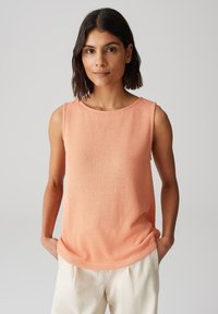 Débardeur sans manches en tissu doux pêche-orange, avec un col rond et une légère finition texturée. Ourlet droit, coupe décontractée.