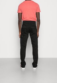 Černé cargo kalhoty s volnějším střihem, vybavené několika bočními kapsami a hladkou texturou, kombinované s korálově zbarvenou krátkým rukávem košilí.