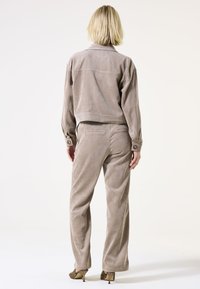 Beige corduroyjack met een cropped ontwerp, gecombineerd met bijpassende broek met hoge taille. Beide hebben een zachte textuur en een relaxed fit.