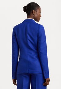 Blazer ajusté bleu vif avec une coupe cintrée, texture lisse et poignets à un seul bouton. Le dos présente un détail de couture subtil.