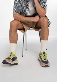 Sportske tenisice s gornjim dijelom od sivog mrežastog materijala, bež nubuk akcentima, svijetlo žutim vezicama i teksturiranim potplatima. U kombinaciji su s bijelim čarapama i šortsem.