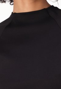 Top negro con un cuello alto, textura suave y ligero detalle en los hombros. La tela parece suave y ajustada.