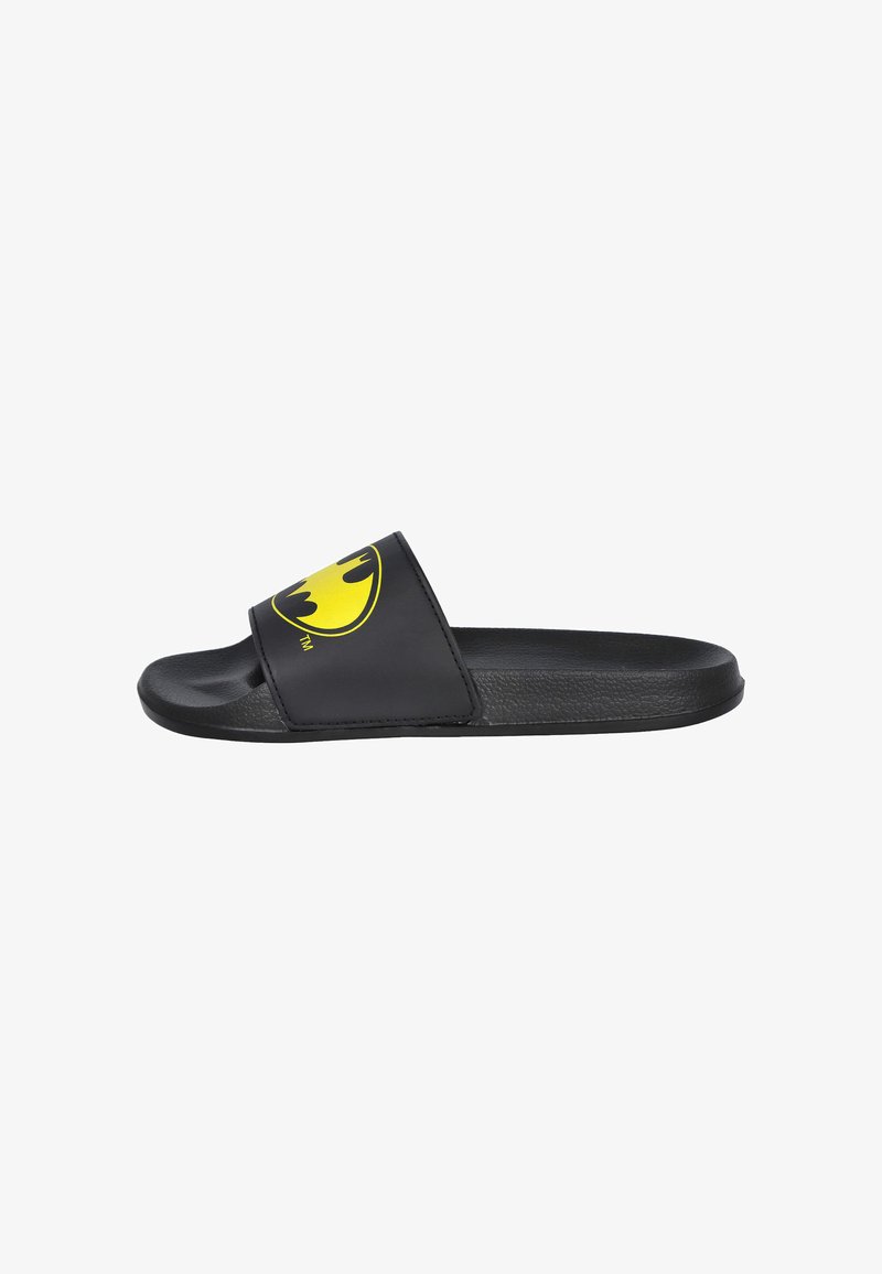Sandalia plana negra con suela plana y tira ancha que presenta el logotipo amarillo de Batman. Fabricada en material sintético suave con un acabado mate.