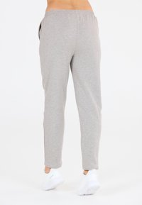Graue, tapered Sweatpants mit einem elastischen Bund, Seitentaschen und einer weichen Textur. Getragen mit weißen Sportschuhen.