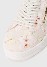 Baskets blanches avec un motif floral texturé en rose clair et crème. Dotées de lacets blancs et d'une fermeture éclair sur le côté.