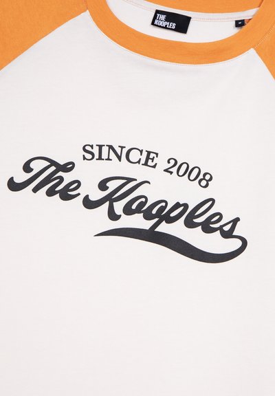 Weißes und oranges T-Shirt mit Raglan-Design. Enthält schwarzen Text: "SINCE 2008" und "The Kooples" in einer Schreibschrift. Aus weichem Baumwollmaterial.