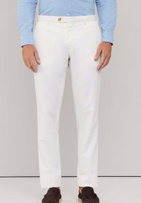 Pantalones de algodón blancos con corte recto, que presentan un cierre de un solo botón, bolsillos laterales y una textura suave. Llevados con zapatillas oscuras.