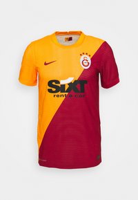 Camisa de fútbol del Galatasaray con diseño dividido, con naranja de un lado y rojo oscuro del otro; incluye el logo de Nike y la marca del patrocinador.