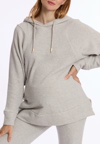 Lichtgrijze hoodie van zacht stof, met een voorzak in kangoeroe-stijl, een trekkoordkap en een losse pasvorm. Verfraaid met gouden hardware.