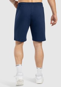 Pantalones cortos deportivos de color navy con una cinturilla elástica y una textura suave, que llegan hasta la mitad del muslo. Llevados con calcetines blancos y zapatillas.