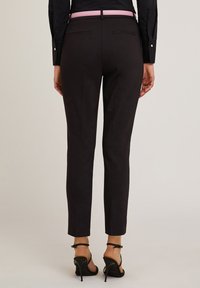 Pantaloni neri su misura con cintura rosa, slim fit, a vita media, con due tasche posteriori e una texture del tessuto liscia. Indossati con tacchi neri.