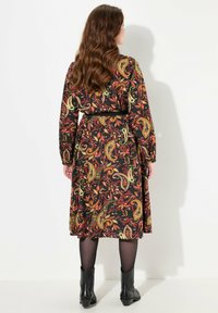 Abito lungo nero con motivo paisley colorato, maniche lunghe, vita cintrata con una cintura nera, abbinato a stivaletti neri.